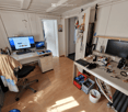 A well-lit room with wooden flooring, two desks, a chair, and various electronic equipment and tools.