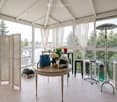 Bright, airy room with large windows and a view, furnished with a round table, stools, a chair, and decorative items.