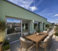 Rooftop terrace with wooden dining table, wicker chairs, potted plants, and city view.
