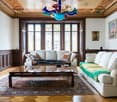 Elegant living room with wooden floors, large stained-glass windows, a colorful chandelier, two sofas, a coffee table, and framed artwork on the walls.