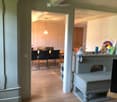 A well-lit hallway leads to a dining area with a table and chairs, and a small sitting area with a stool and decorative items.