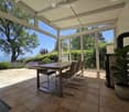 Bright, airy dining area with large glass walls offering a scenic view, featuring a wooden dining table, chairs, a fireplace, and a potted plant.