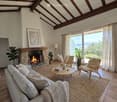 Living room with exposed wooden beams, fireplace, sofa, coffee table, and large windows offering a scenic view.