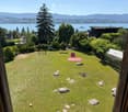 Lush green garden with scattered rocks, a yoga mat, a small table, and a view of a lake and distant mountains.