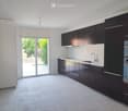Modern kitchen with dark cabinets, white countertops, and a built-in oven. Features a large window with a view of greenery outside.