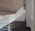 Modern hallway with wooden slatted ceiling, white walls, dark concrete floor, and white metal railings leading to an open area.
