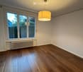 Empty room with wooden flooring, large windows, radiator, and a hanging light fixture.