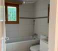 Modern bathroom with a bathtub, toilet, sink, and showerhead. Grey tiled walls and wooden ceiling.