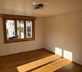 Empty room with wooden flooring and large windows, allowing natural light to fill the space.