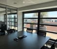 Modern office space with large windows, black conference table, chairs, laptop, and office equipment.
