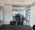 Modern office space with large glass partitions, black conference table, and several chairs.