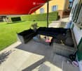 Balcony with a black wicker sofa and coffee table, overlooking a well-maintained lawn and garden.