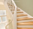 Spiral staircase with wooden steps and white balustrade, light green walls, frosted glass windows on the left side.
