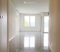 Empty hallway with white walls, polished tile floors, and recessed lighting. Features a window and a glass door leading to an outdoor area.