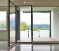 Open hallway with large glass doors leading to a balcony, offering a scenic mountain view and greenery.