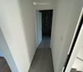 A narrow hallway with white walls and tiled floor, leading to a small shower area with a showerhead and controls.