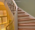 Spiral staircase with wooden steps and white balustrade, leading to an upper level. The walls are painted in a light green color, and the floor is tiled.