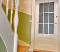 Hallway with a staircase leading upwards, green and beige walls, wooden steps, white balusters, and a frosted glass door at the end.