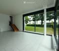 Bright, minimalist room with large glass windows, white tiled floor, and a wooden staircase leading upwards.