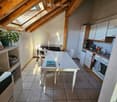 Bright kitchen with white cabinets, a dining table with chairs, and modern appliances including a refrigerator and oven. The room features exposed wooden beams and a skylight, with a small plant on a shelf.
