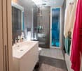 Modern bathroom with a white sink, chrome faucet, large mirror, toilet, glass-enclosed shower, and towels hanging on the wall.