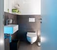 Modern bathroom with a white toilet, a light blue sink, a chrome faucet, and neatly arranged towels on shelves.