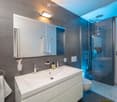 Modern bathroom with a large sink, mirror, and a glass-enclosed shower. Features include a towel rack, toothbrush holder, and a sleek design with grey tiles.