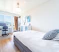Bright bedroom with a large bed, desk with chair, and a view of the mountains through large windows and a sliding door.