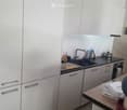 Modern kitchen with white cabinets, black countertop, sink, and various cleaning supplies. Includes an oven and a frying pan on the counter.