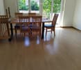 Dining room with wooden floor, dining table, and chairs, large windows with a view of greenery.