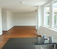 Empty room with white walls, wooden flooring, and large windows allowing natural light. No furniture or equipment present.