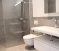 Modern bathroom with a white sink, chrome faucet, toilet, and a glass-enclosed shower area with a built-in seat.