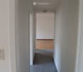 Empty hallway with tiled floor and white walls, leading to another room with wooden flooring visible at the end.