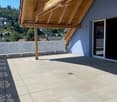Balcony with wooden roof, tiled floor, white railing, and large window opening to the interior.