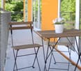 Balcony with a small wooden table, two folding chairs, and a white flower pot on the table.