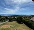 Panoramic view of a rural landscape with houses, trees, and distant mountains under a clear blue sky.