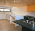 Modern kitchen with black countertops, stainless steel sink, stove, and orange cabinets.
