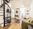Modern living room with a spiral staircase, sofa, coffee table, small table, and television mounted on the wall.