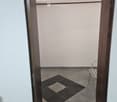 A small, tiled room with a single chair near the door. The floor features a black and gray checkered pattern in the center, surrounded by gray tiles.