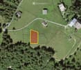 Aerial view of a rural property with multiple buildings, including houses and outbuildings, surrounded by green fields and trees. The highlighted area in yellow indicates a specific plot or lot.