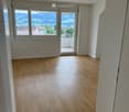 Empty room with wooden flooring, large windows, and a sliding glass door leading to a balcony.