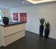 Modern hallway with dark tiled floor, white walls, reception desk, two vases with plants, and two abstract paintings.
