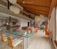 Open-plan living and dining area with a glass dining table, modern chairs, a sofa, kitchen area with counter and stools, and decorative items including a guitar and a flower vase.