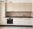 Modern kitchen with light-colored cabinets, black countertops, and stainless steel appliances including an oven and sink.