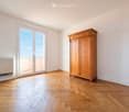 Bright, unfurnished room with wooden flooring, large window offering a view, and a wooden wardrobe.