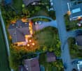 Aerial view of a residential area with multiple houses, well-lit driveways, parked cars, and landscaped gardens.
