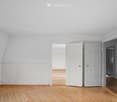 Empty room with light-colored walls, wooden herringbone flooring, and several open doors leading to adjacent spaces.