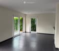 Empty room with dark tiled floor, white walls, and large glass sliding doors leading to a green outdoor area.