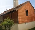 Two-story house with wooden siding and red-tiled roof, featuring multiple chimneys and windows.