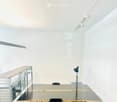 Modern, minimalist room with a large glass table, black chair, metal shelving unit, and track lighting.